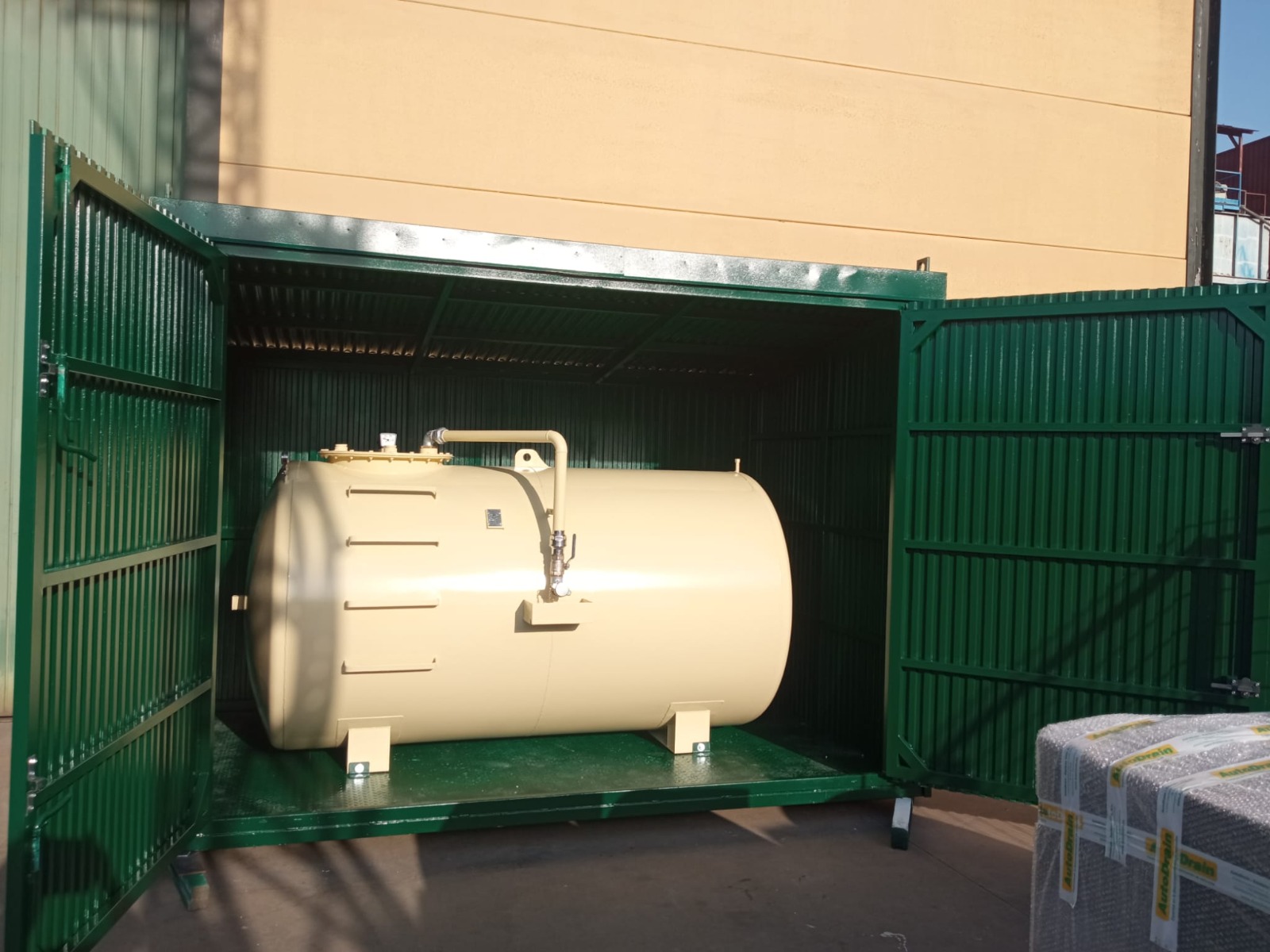 Depósito beige instalado dentro de una caseta metálica verde con las puertas abiertas y bandeja de recogida