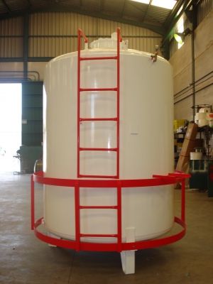 Depósito cilíndrico vertical blanco con escalera y barandilla rojas en el taller