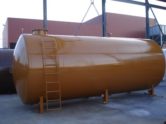 Depósito cilíndrico horizontal con imprimación ocre, suspendido de una grúa junto a la nave